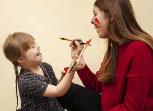 Kind mit Down Syndrom und Betreuerin malen sich gegenseitig ihre Gesichter an